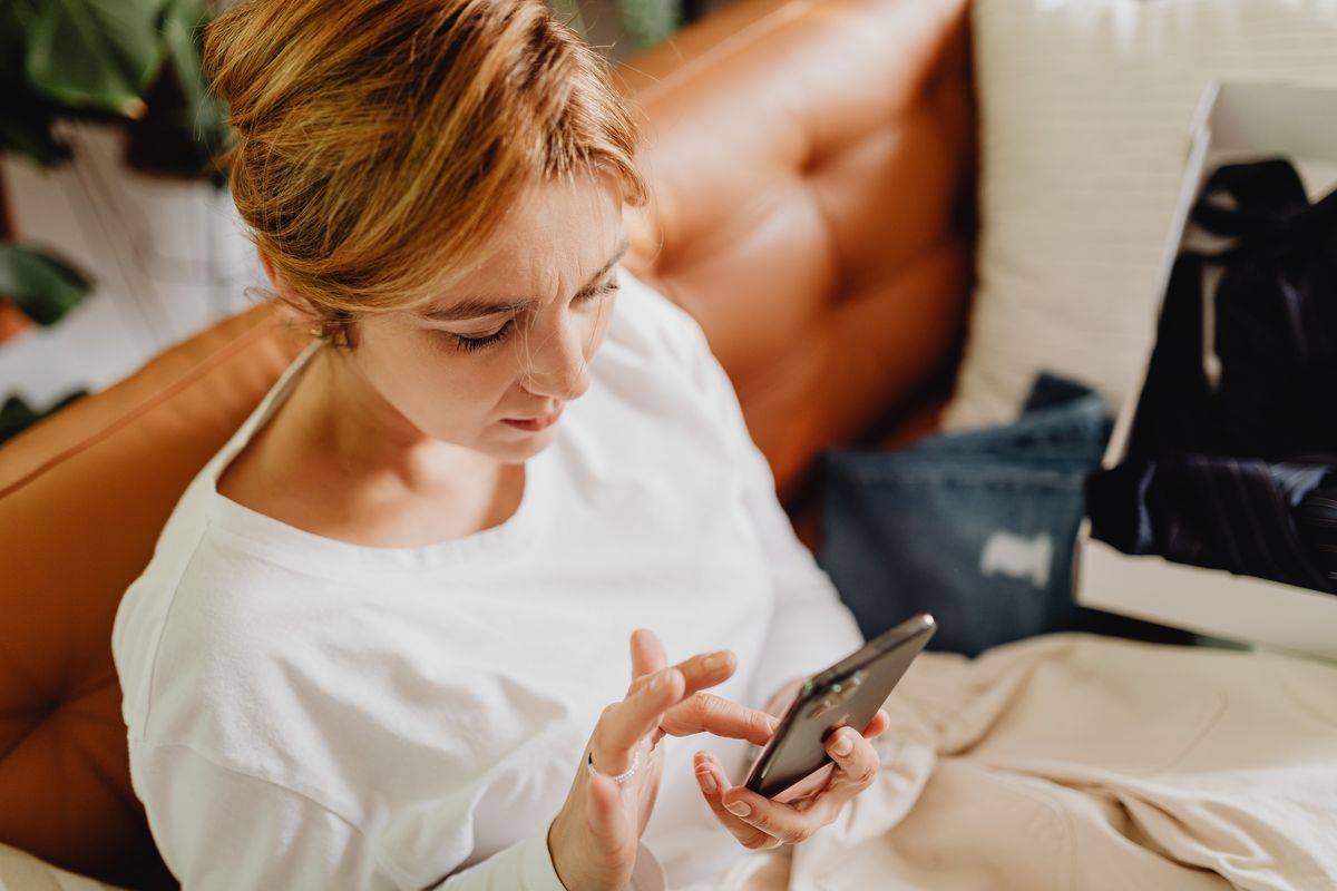 Junge Frau auf dem Sofa mit Smartphone, Nachsorge nach der Reha